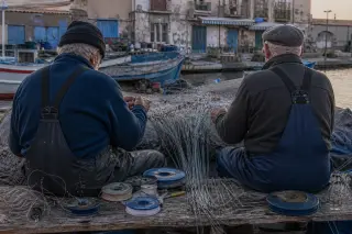 Two elderly fishermen quietly repairing palangrotte fishing lines on a weathered port bench at dawn, rustic boats and nets in the background, captured in soft Mediterranean light.
